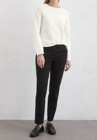 White long-sleeve sweater with a round neck, paired with fitted black pants and black loafers, creating a simple and neutral outfit.