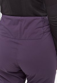 Pantalons techniques violets avec une texture lisse, une taille élastique et une coupe ajustée. Design minimaliste sans logos ni motifs visibles.