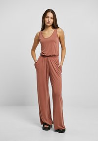 Rosa jumpsuit med scoop-neck og elastisk midjebånd, med vide ben og sidelommer, laget av myk stoff.