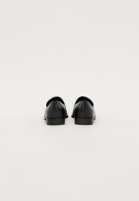 Mocasines de cuero negro con una textura suave, punta redondeada y un tacón modesto. La parte trasera presenta un diseño de corte sutil cerca de la parte superior.