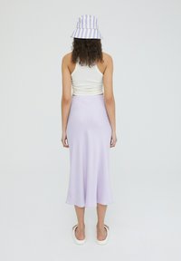 Lila midi-rok gemaakt van soepel, lichtgewicht stof. Gecombineerd met een aansluitend wit tanktop en een blauwgestreepte bucket hat, gedragen met platte sandalen.