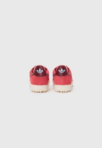Red suede sneakers with a beige rubber sole. Features a maroon heel with blue logo detail. Back view showcasing stitching and design accents.