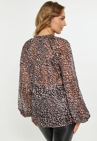 Durchsichtige schwarze Bluse mit floralem Muster in Rosatönen und Gold, ausgestattet mit puffartigen langen Ärmeln und einem gerafften Ausschnitt für zusätzlichen Textur.