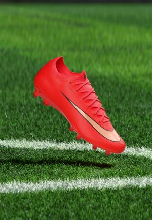 Roter Fußballschuh mit metallischem Swoosh-Logo schwebt über einer weißen Linie auf grünem Rasen.