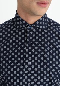 Marineblauw overhemd met knopen, voorzien van een patroon van witte strepen en stippen, klassieke kraag, gladde stof en twee zichtbare knopen aan de voorkant.