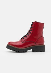 Bottes courtes en cuir verni rouge avec lacets noirs, semelle en caoutchouc épaisse noire, bout arrondi et coutures contrastées.