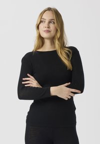 Svart langermet topp med rund hals, myk tekstur og tettsittende design. Modellen krysser armene i en nøytral positur mot en ensfarget bakgrunn.