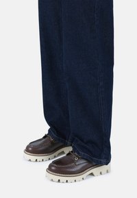 Tumedast sinisest denimist püksid ja pruunid nahast kingad, millel on paks koorevärvi tall ja esiosas paelte detail.