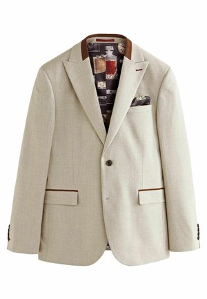Blazer de color beis claro con una tela texturizada, solapas marrones y dos bolsillos frontales. El forro interior presenta patrones de fotografías vintage y objetos.