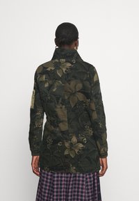 Zelená bunda s květinovým vzorem, límcem, dlouhými rukávy a žebrovanými manžetami. Vyrobena z texturované látky s různými rostlinnými motivy.