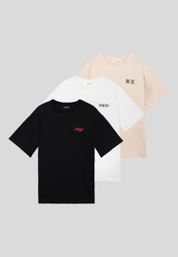 Τρία κοντομάνικα t-shirts με στρογγυλή λαιμόκοψη σε μαύρο, λευκό και μπεζ, το καθένα με το κείμενο "Tokyo" σε διαφορετικά σχέδια στο στήθος.