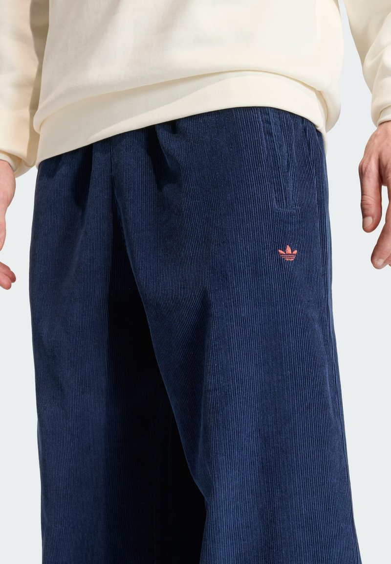 Navy corduroy trousers featuring a textured surface and side pockets, accented with a small pink embroidered logo on the front.