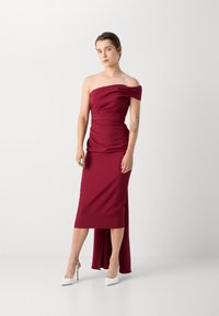 Rochie burgundy fără bretele, cu un decolteu drapat și o siluetă ajustată, având o fante înaltă și un material moale. Asortată cu tocuri înalte albe.