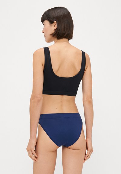 Melna sporta krūšturis ar platām siksnām un zemu aizmuguri. Saskaņots ar tumši zilu bikini tipa apakšveļu, kas izceļas ar gludu tekstūru un minimālām vīlēm.