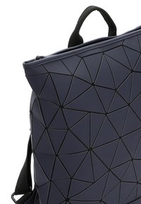 Marinblå geometrisk väska med en strukturerad yta i plast. Har ett övre handtag och justerbar rem för mångsidig bärning.