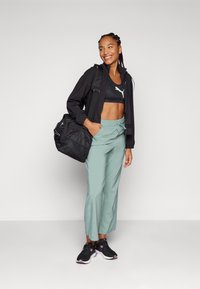 Chaqueta negra con cremallera, sujetador deportivo negro, pantalones de pierna ancha verde menta, zapatillas negras con detalles rosas y una bolsa de gimnasio negra.