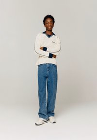 Un pull en laine crème avec un col et des poignets en marine, associé à un jean en denim bleu décontracté et des baskets blanches avec des accents noirs.