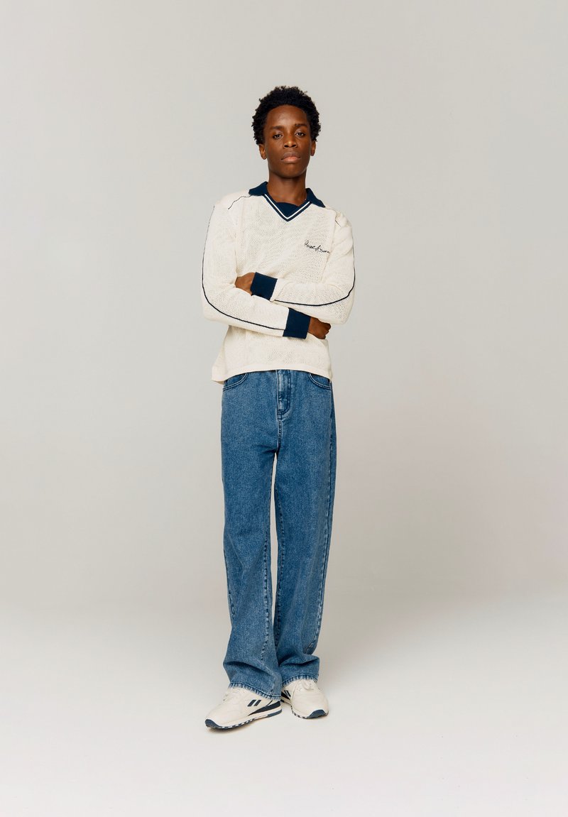 Un pull en laine crème avec un col et des poignets en marine, associé à un jean en denim bleu décontracté et des baskets blanches avec des accents noirs.