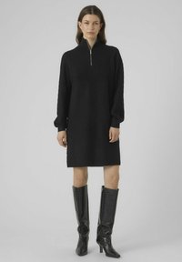 Abito nero con zip, caratterizzato da un motivo testurizzato e maniche lunghe, abbinato a stivali neri alti fino al ginocchio in glossy con un design a rilievo che simula la pelle di coccodrillo.