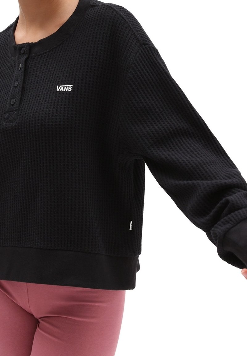 Zwarte wafelstructuur lange mouwen top met henley-halslijn en logo-detail. Heeft een cropped ontwerp en ribgebreide manchetten bij de polsen.