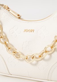 White textured leather handbag featuring embossed floral patterns, a gold chain strap, and a gold zipper with a branded pull tab.