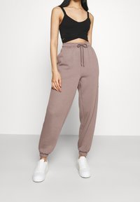 Pantaloni della tuta color marrone chiaro con vita elastica e polsini, abbinati a un top corto nero e sneakers bianche. Tessuto morbido.