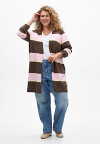 Cardigan rayé aux couleurs marron, rose et jaune, avec une coupe ouverte à l'avant, des manches longues et des poignets côtelés, associé à un jean bleu taille haute.
