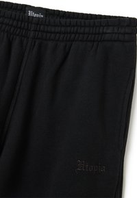 Zwarte sweatpants van zacht materiaal met een elastische tailleband. Bevat een geborduurd "Utopia" logo in donkere thread nabij de onderkant.