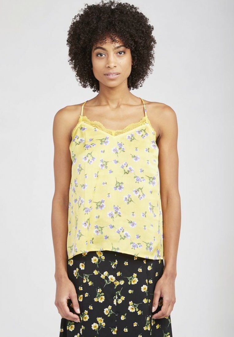 Camisole floral jaune avec des bordures en dentelle et des fines bretelles, ornée de fleurs violettes sur un tissu doux. Associée à une jupe noire à motifs floraux.