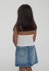 Top bianco senza spalline con dettaglio lacciato sul retro, abbinato a una gonna di jeans con due tasche posteriori e orlo sfilacciato.
