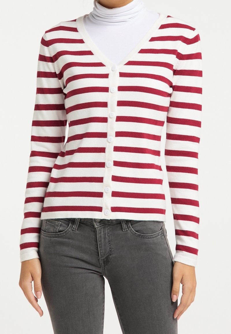 Femme portant un cardigan boutonné à rayures horizontales rouges et blanches par-dessus un col roulé blanc, associé à un jean gris foncé.