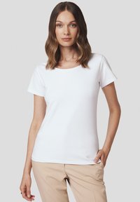 Biała koszulka z krótkim rękawem i okrągłym dekoltem, wykonana z gładkiego materiału, dopasowana sylwetka, w połączeniu z jasnobeżowymi spodniami.