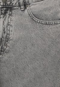 Gros plan sur un tissu en denim gris avec une poche avant, une passants de ceinture, un bouton et un détail de rivet en métal.