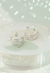 Boucles d'oreilles en argent présentant un design ondulé avec plusieurs brins et une rangée de petites pierres transparentes. Fini poli avec fermetures à poussoir.