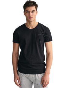 Svart bomull t-skjorte med rund hals og korte ermer. Har en subtil logo på brystet. Modellen har på seg grå joggebukser.