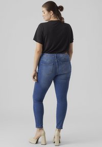Blue denim skinny jeans with back pockets, paired with a black t-shirt. The model wears beige platform heels, showing leg details.