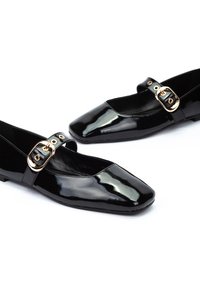 Bailarinas de charol negro con un diseño de punta cuadrada, que cuentan con una correa en el empeine con un detalle de hebilla dorada. Textura suave y brillante.