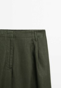 Oliivinvihreät pellavahousut litteällä etuosalla, joissa on sivutaskut ja vyölenkit. Kankaan pinta on sileä ja kevyt.