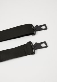 Két fekete nylon heveder fekete fém forgóhoroggal, "RAINS" márkájú, egy fehér felületen fektetve.