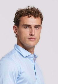 Lichtblauw poloshirt met een kraaghalslijn, korte mouwen en knoopdetails. De stof lijkt soepel en iets getailleerd.