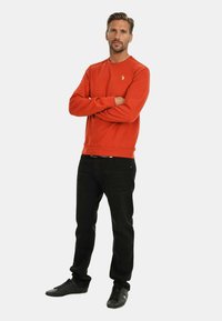 Rotes Sweatshirt mit rundem Ausschnitt und kleinem Logo. Kombiniert mit schwarzen Jeans und schwarzen Turnschuhen. Einfaches, lässiges Design.