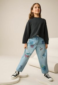 Lyseblå denimjeans med farverige blomster- og frugt mønstre foran, parret med en antracitgrå oversized sweatshirt med lange ærmer og sorte sneakers.