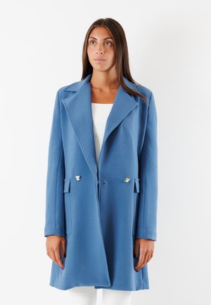 Cappotto lungo blu con colletto strutturato, tasche laterali e dettagli metallici. Tessuto liscio e vestibilità morbida, che arriva a metà coscia.