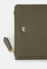 Portefeuille en cuir texturé vert olive avec quincaillerie dorée, arborant un petit accent logo et une fermeture éclair. Forme carrée avec bords cousus.