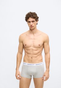 Sive bombažne bokser hlače z belim pasom, na katerem je napis "GANT" v mornarsko modri barvi. Tkanina je videti mehka in gladka.