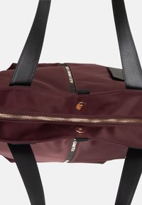 Borsa tote in tessuto bordeaux con manici in pelle nera, dotata di una zip dorata, accessori in oro rosa e finitura testurizzata, che mette in risalto un design minimalista.
