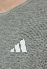 Un tejido de color gris con una superficie texturizada presenta un logotipo blanco de tres franjas en la esquina inferior derecha.