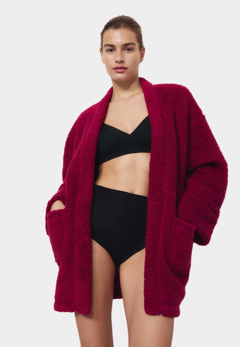 Cardigan de gran tamaño en un fucsia difuso con bolsillos, usado sobre un bralette negro y un bikini de tiro alto, que ofrece una apariencia suave y texturada.