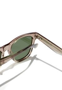 Ochelari de soare cu nuanță maro și lentile verzi. Rame pătrate supradimensionate din acril transparent. Accente metalice pe braț.
