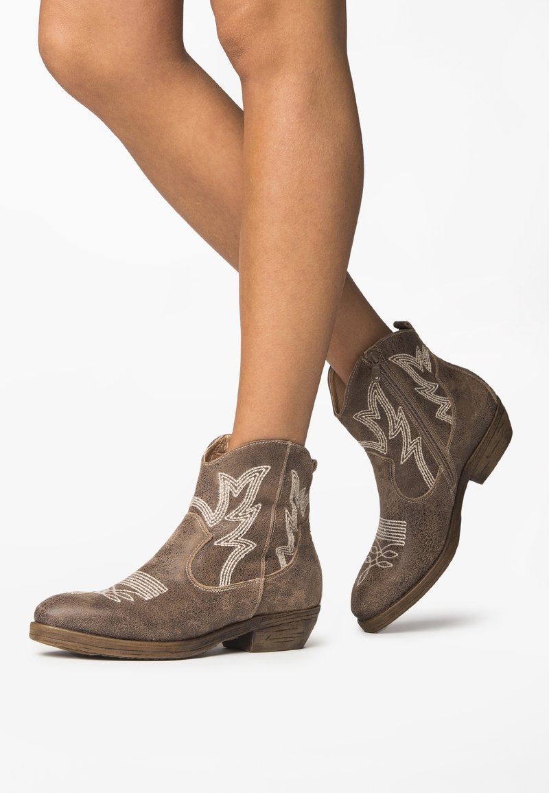 Bruna mockakängor i ankellängd med vita broderade mönster, som har en låg klack och en spetsig tå. Dekorerade med sömnadsdetaljer.